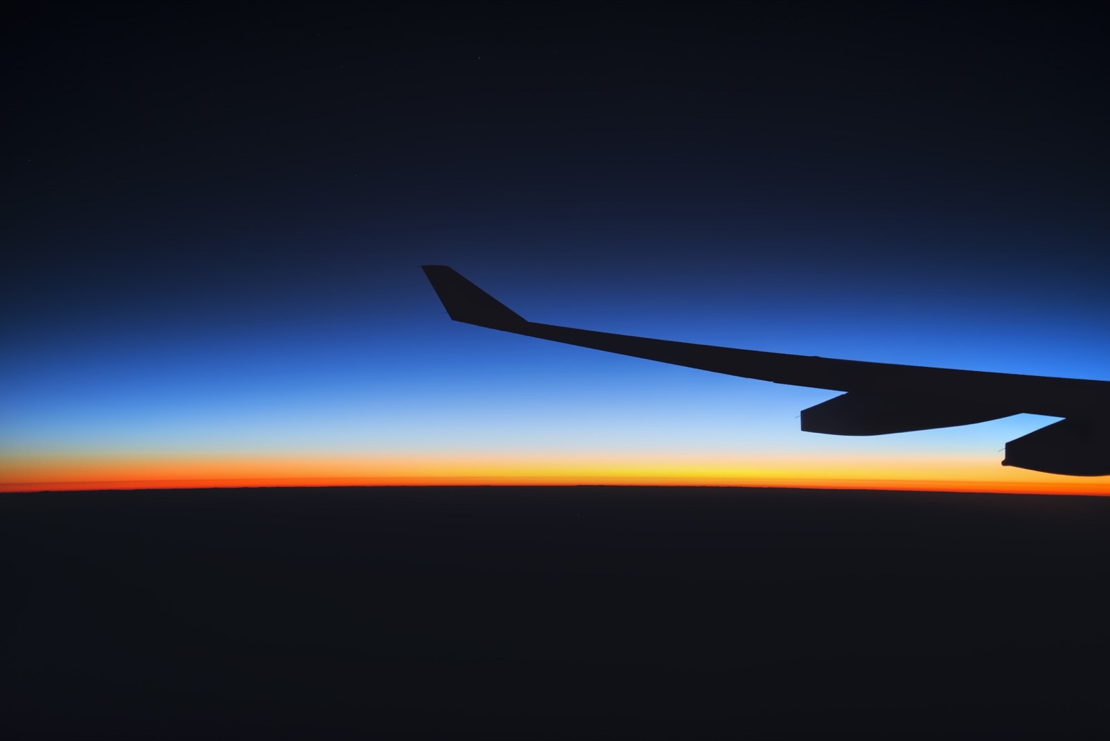 機窓から見える夜明けの空と翼のシルエット